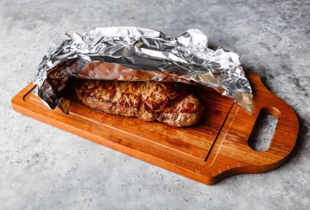 bistecca alla griglia appoggiata su tavola di legno ricoperta di foglio di alluminio - strip steak aluminum foil steak foto e immagini stock