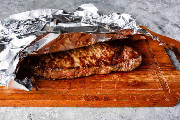 bistecca alla griglia appoggiata su tavola di legno ricoperta di foglio di alluminio - strip steak aluminum foil steak foto e immagini stock