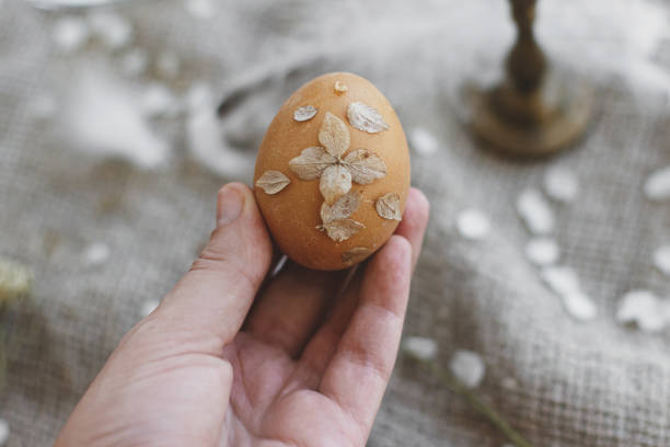 istock Hand holding Easter egg decorated with dry flower petals on rustic linen napkin and cherry bloom 1302585291