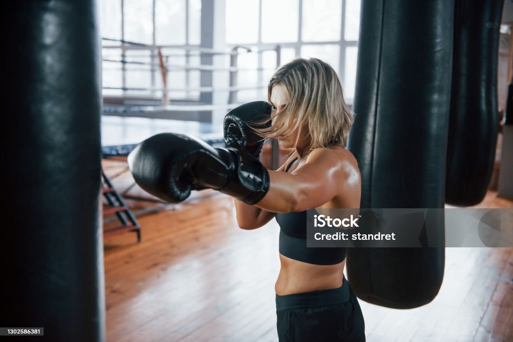 Need to be strong. Female boxer is punching the bag. Blonde have exercise in the gym Need to be strong. Female boxer is punching the bag. Blonde have exercise in the gym. Kickboxing Stock Photo