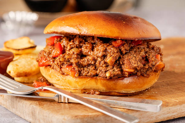 Sloppy Joe Sandwich With French Fries. Close-up Sloppy Joe sandwich on plate with fries on a counter top. Sloppy Joe’s, the story goes, started in a bar by the same name, ground beef with peppers, onion, chilli maybe and a tomato sauce was put together in a burger bun as a quick snack, served with fries and extra sauces such as ketchup or brown sauce, the rest is history. Colour horizontal with some copy space. sloppy joes stock pictures, royalty-free photos & images