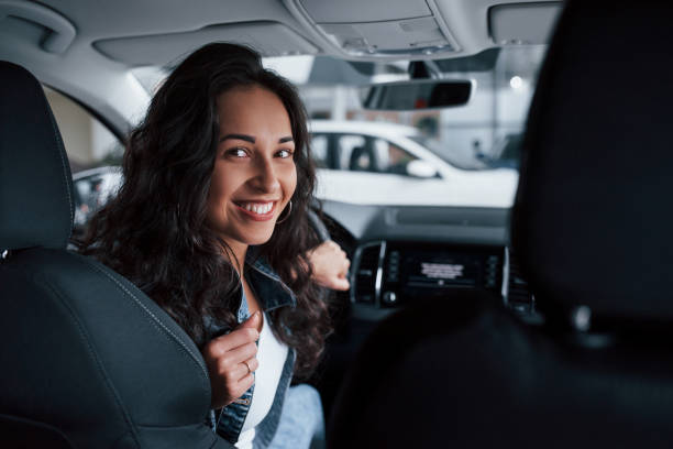 Positive emotions. Cute girl with black hair trying her brand new expensive car in the automobile salon Positive emotions. Cute girl with black hair trying her brand new expensive car in the automobile salon. saloon car stock pictures, royalty-free photos & images