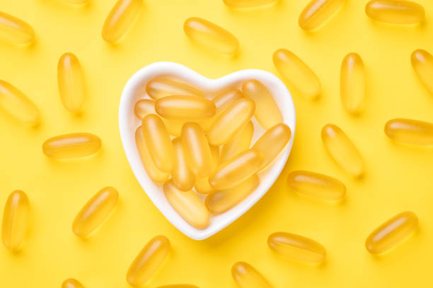 le capsule di olio di pesce vitamina d e omega 3 si integrano in una piastra a forma di cuore su sfondo giallo. concetto di assistenza sanitaria. vista dall'alto - fatty acid foto e immagini stock