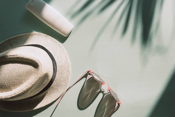 istock Sun hat, glasses and spf cream or lotion unbranded package on light blue background with palm tree leaf shadow, top view 1302590881