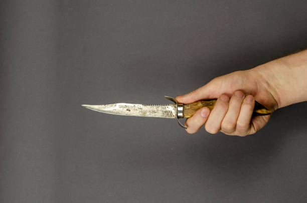 istock Hand holds a hunting knife on a gray background. 1302592018