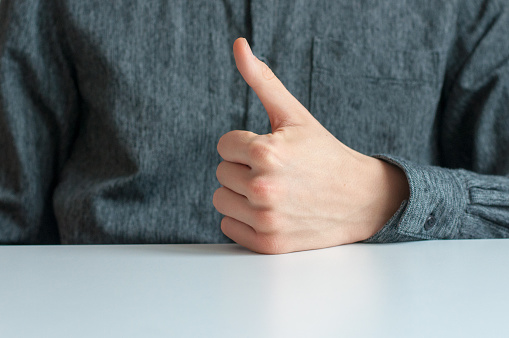 Closeup of male hand showing thumbs up sign against grey background.