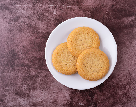 Top view of three soft sugar cookies on a white plate atop a red mottled background illuminated with natural lighting.