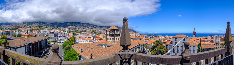 Panoramic view over the rooftops of Funchal the capitol of Madeira island during a beautiful summer day with the mounains on one side and the ocean on the other.