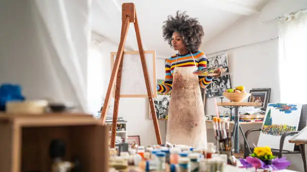 Photo of Afro fine art painter drawing in studio, holding color palette.