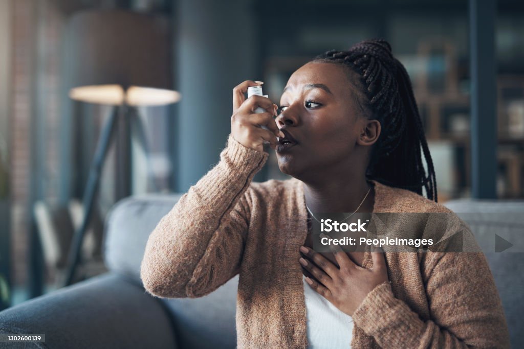 My chest is closing up! Cropped shot of an attractive young woman using a pump during an asthma attack in her living room Asthmatic Stock Photo