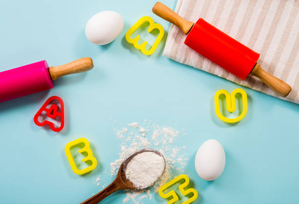 istock Fun cooking class for kids border concept lot of room for text. Eggs, flour, rolling pins, letter shape cookie cutters on light blue background, studio shot. 1302600607
