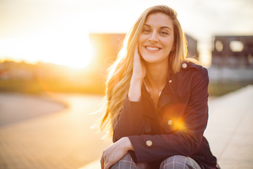 Beautiful young woman enjoying quiet moment at golden hour. She is spending time outside and is smiling while sunbeam shines behind her.