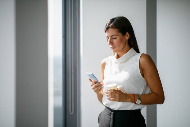 istock Beautiful businesswoman using mobile phone by the office window on a coffee break 1302602721