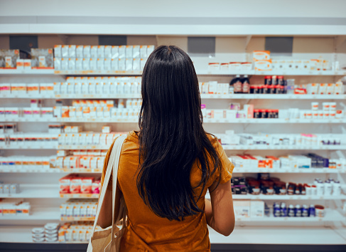 Vista trasera de la joven con una bolsa contra el estante en la farmacia en busca de medicina photo