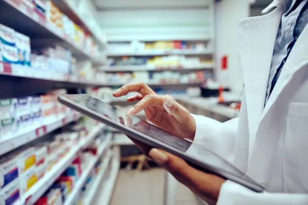Photo of Closeup of hands of young female pharmacist checking inventory in medical store using digital tablet