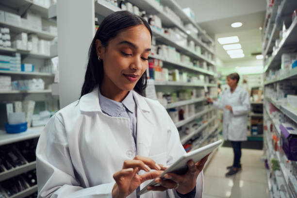 giovane lavoratrice sorridente in farmacia che indossa un labcoat che controlla l'inventario utilizzando tablet digitale - prescription medicine foto e immagini stock