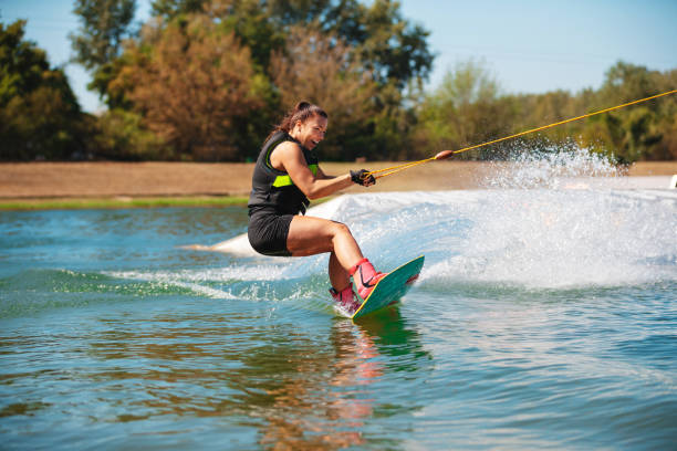 Smiling young woman tilting wakeboard upwards and spraying stock photo