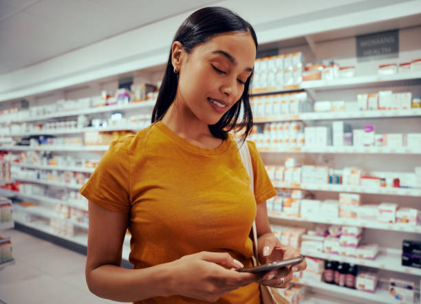 istock Young woman using smartphone standing against shelf in pharmacy 1302606997