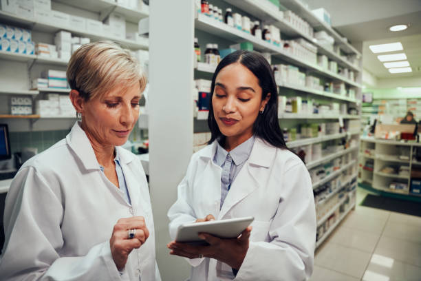 istock Happy young female pharmacist discussing work with senior colleague using digital tablet in chemist 1302607167