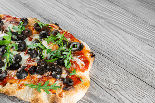 Pinsa romana gourmet italian cuisine on grey wooden background. Scrocchiarella traditional dish. Food delivery from pizzeria. Pinsa with meat, arugula, olives, cheese.