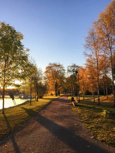 Pathway next to river. Park in small town, Karlstad, Sweden. Autumn colours and sunlight.