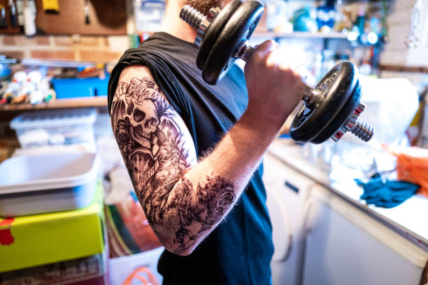tattoo guy lifting weights in his garage - muscular build men tattoo human arm imagens e fotografias de stock