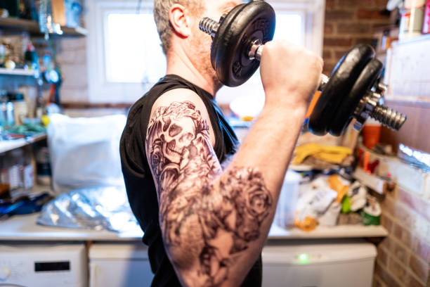 tattoo guy lifting weights in his garage - muscular build men tattoo human arm imagens e fotografias de stock