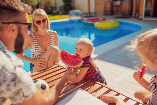 istock Father feeding baby boy with watermelon slice by the pool 1302614242