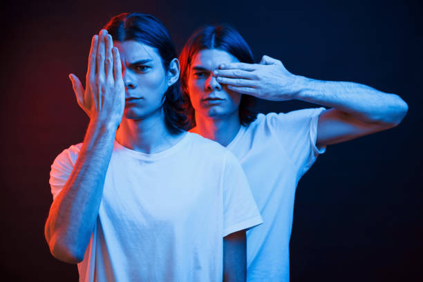 couvrant les yeux avec les mains. portrait de frères jumeaux. studio tiré dans le studio foncé avec la lumière de néon - seeing double photos et images de collection