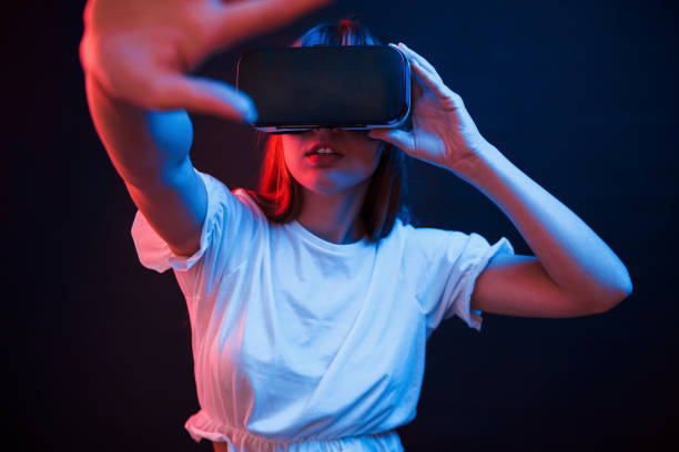 istock It's quite interesting. Young woman using virtual reality glasses in the dark room with neon lighting 1302616124