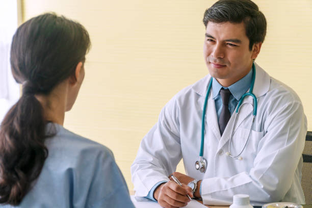 istock Doctor man wear uniform with pen and stethoscope sitting in office while talking about problem health patient woman fell friendly. Patient young woman listen advice doctor. Health-care concept. 1302617298
