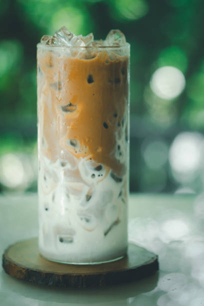istock Ice coffee latte on a wooden table with coffee being poured into it showing the texture and refreshing look of the drink. Iced coffee in a tall glass. 1302617721
