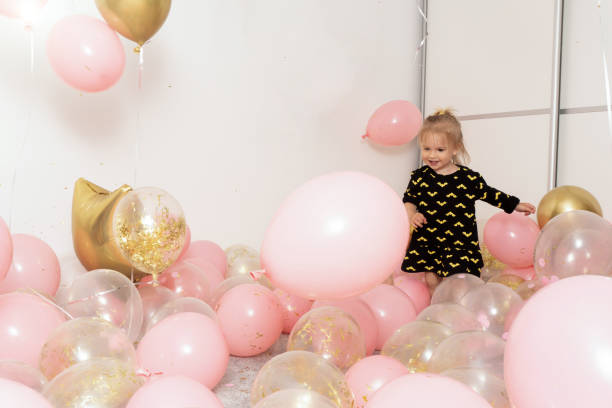 celebração de festa de aniversário infantil, balões rosa e dourado por toda parte, feliz menina caucasiana pulando e brincando, fundo de parede branca, espaço de cópia. - birthday present family facial expression birthday - fotografias e filmes do acervo