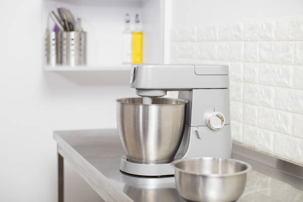 Small Electric Kitchen Appliances. Modern silver kitchen stand mixer in light cozy confectionery. A closeup of Multi-Task Blender mixing dough, and Stainless Steel bowl on the table.