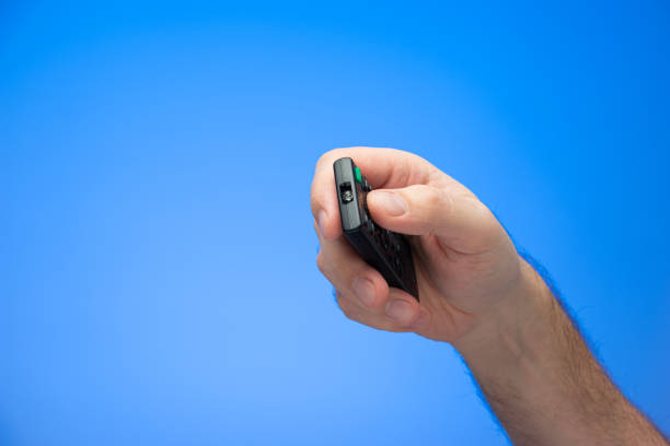 istock Caucasian male hand holding and pressing buttons on a digital remote control angled towards the camera isolated on blue 1302622432