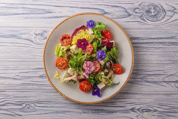 Beautiful healthy spring salad decorated with flowers Vegetarian salad with tomato, lettuce, and cheese garnished with edible flowers. Spring food concept. edible flower stock pictures, royalty-free photos & images