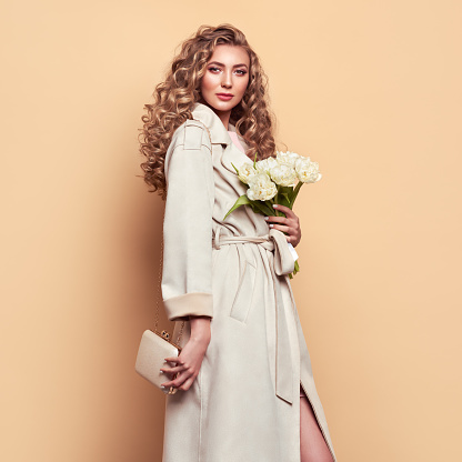Young elegant woman in trendy white coat. Blonde hair, coral dress, isolated on beige background, studio shot. Fashion spring lookbook. Model woman with handbag