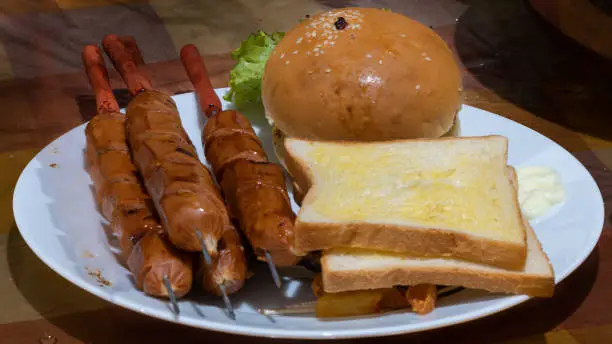 Photo of Cheeseburger with sausages and sliced bread with butter on a plate, delicious mouth-watering dinner is ready to eat.