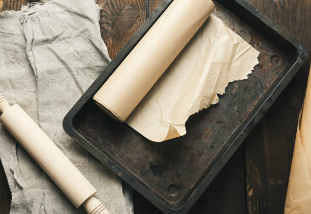 empty rectangular metal pan covered with brown parchment paper and paper rolls empty rectangular metal pan covered with brown parchment paper and paper rolls on a wooden table, top view wax paper stock pictures, royalty-free photos & images