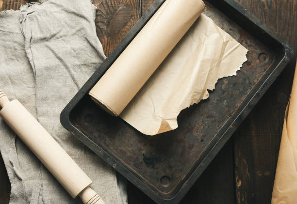 пустая прямоугольная металлическая кастрюля, покрытая коричневой пергаментной бумагой и бумажными рулонами - baking paper cookie tray стоковые фото и изображения