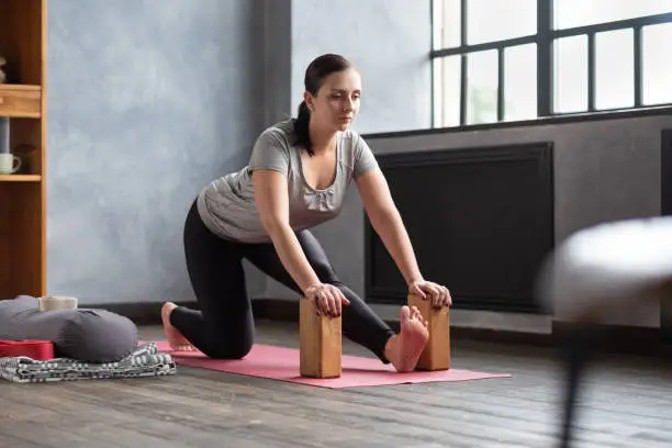 Photo of woman doing stretching exercise using props, block, Ardha Hanumanasana