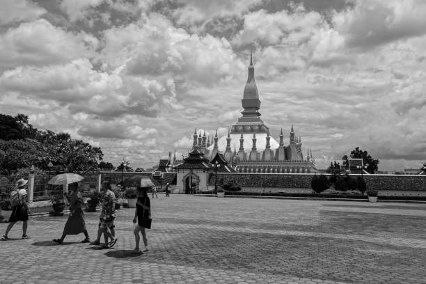 Robed Buddhist monk walking in front of Pha That Luong Golden Stupa in Vientiane, Laos. Vientiane, Vientiane, Laos-September 1, 2018:Robed Buddhist monk with an umbrella, walking in front of Pha That Luong Great Sacred Stupa in Vientiane, Laos. black and white travel travel destinations monk stock pictures, royalty-free photos & images