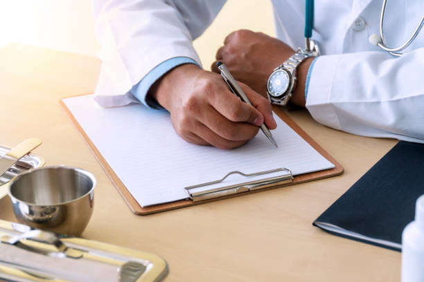 istock Doctor man holding pen ready to make notes only hands seen on table workplace. Doctor hand hold silver pen on patient with paper report on clipboard, physical check patient. Healthy lifestyle concept. 1302631558