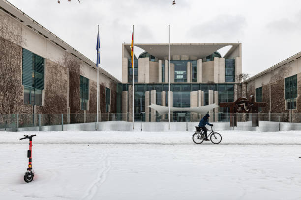one person on bicycle passing the German Chancellery building in Berlin in the snow Berlin, Germany - February 9, 2021: one person on bicycle going by the German Chancellery building in Berlin at a gray snowy winter day chancellor of germany photos stock pictures, royalty-free photos & images
