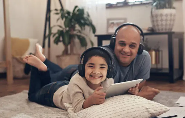 Shot of an adorable little boy using a digital tablet and headphones with his father at home