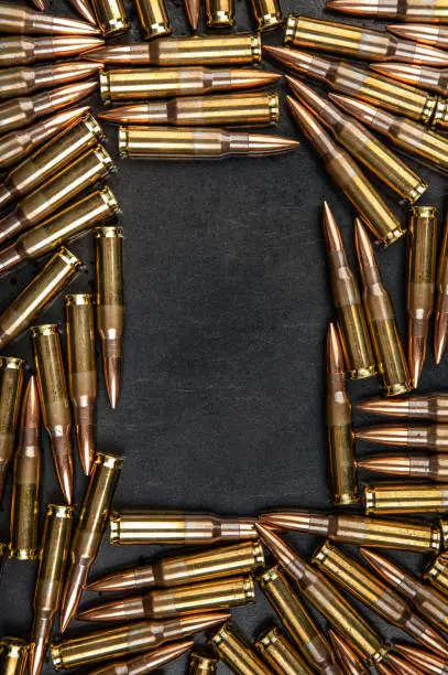 Photo of Background from rifle cartridges on a gray metal background. Copy space for text in the center of the image in the form of a rectangle.