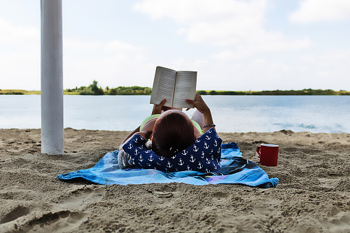 Relaxed woman enjoying a day at the beach and reading a book.