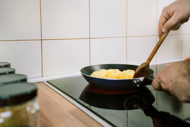 istock Preparing eggs for breakfast. Overhead view of black kitchen stove with frying pan. 1302640770
