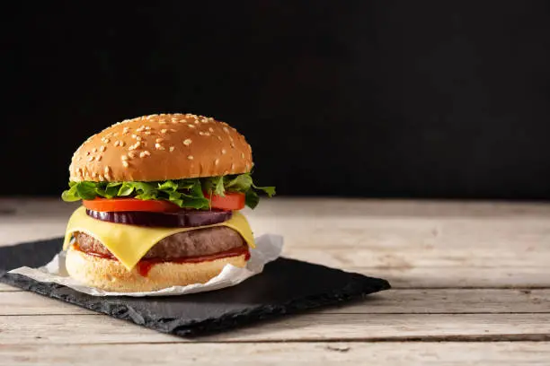 Cheeseburger with beef,tomato, lettuce and onion on wooden table