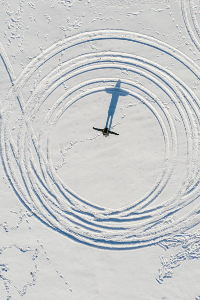 I am a bird. Man standing on a snow casting bird shaped shadow, directly above aerial view